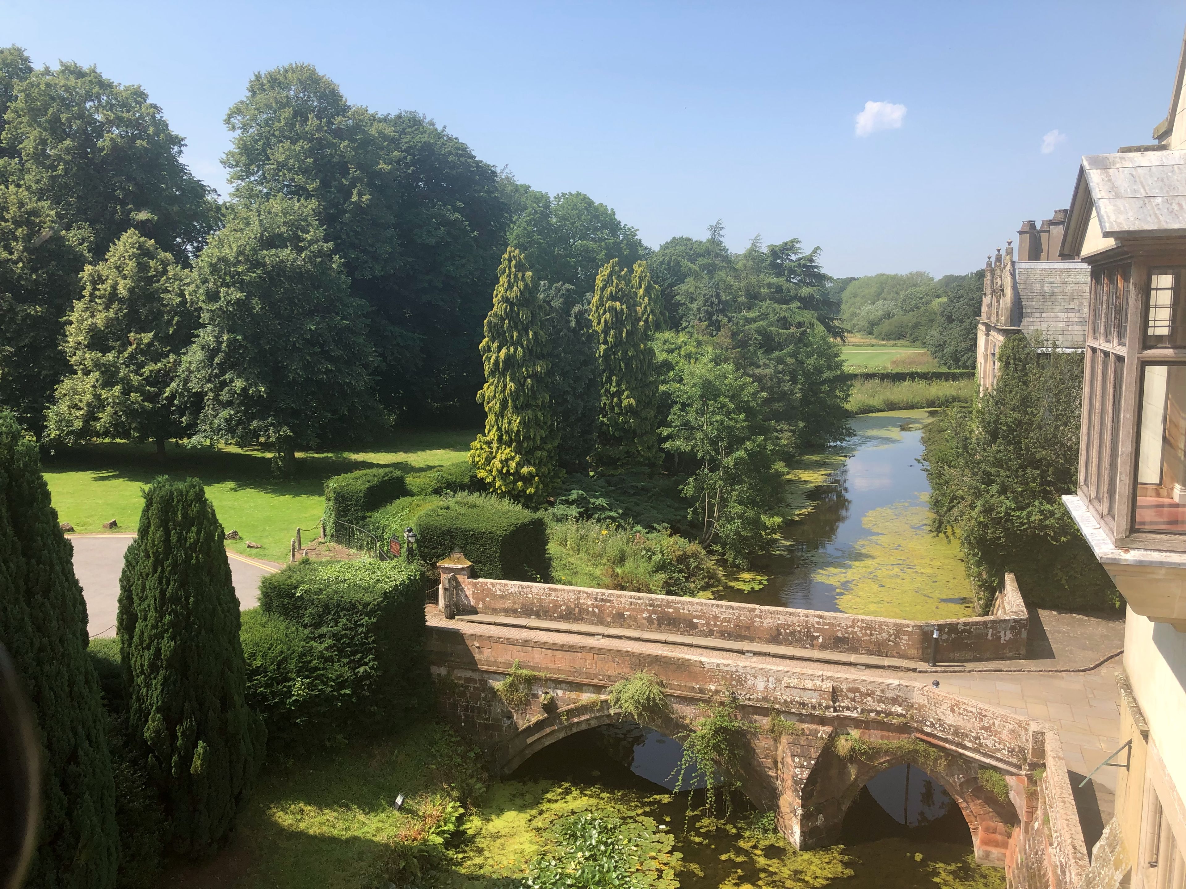 A historic stone bridge over a calm river, surrounded by lush greenery and trees.