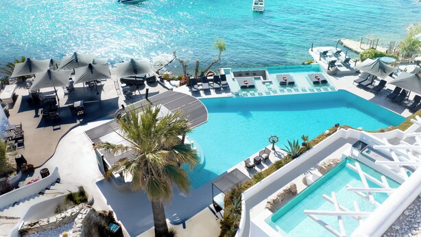 A resort with a large central pool, sun loungers, and a palm tree. - Kivotos Mykonos - Preferred Hotels & Resorts (Mykonos)