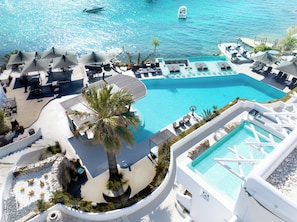 A resort with a large central pool, sun loungers, and a palm tree.