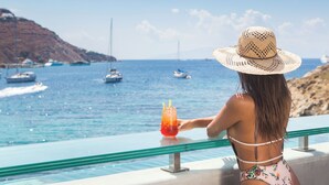 A person in a swimsuit and straw hat overlooking a pool with a view of boats and a rocky coastline. - Kivotos Mykonos - Preferred Hotels & Resorts (Mykonos)