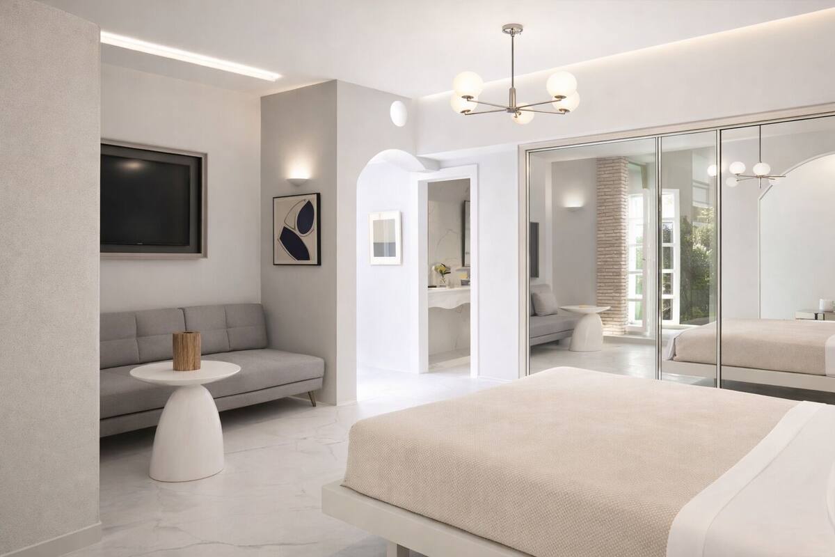 Een moderne slaapkamer met een groot bed, een bank, een klein rond tafeltje en een grote spiegel.