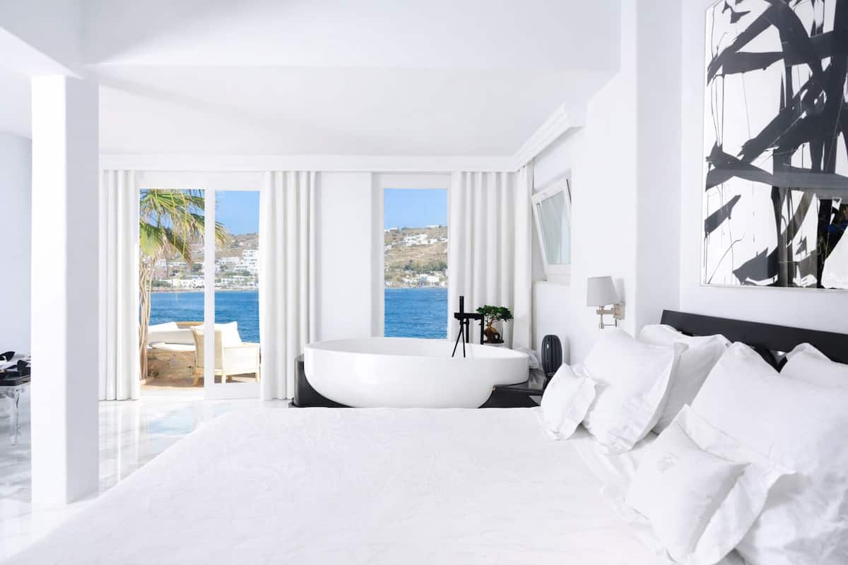Een moderne hotelkamer met een groot bed, een badkuip en een balkon met uitzicht op zee.