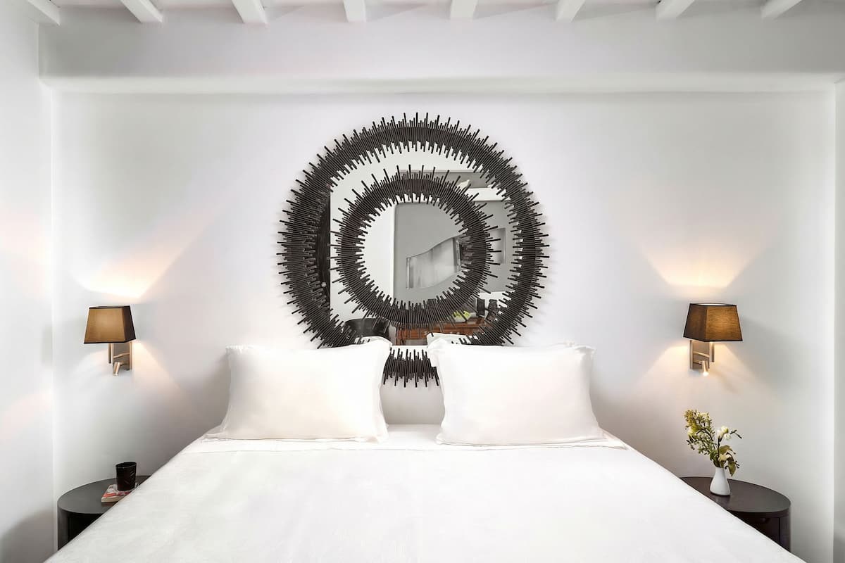 Een slaapkamer met een groot bed, twee nachtkastjes, een spiegel aan de muur en twee wandlampen.