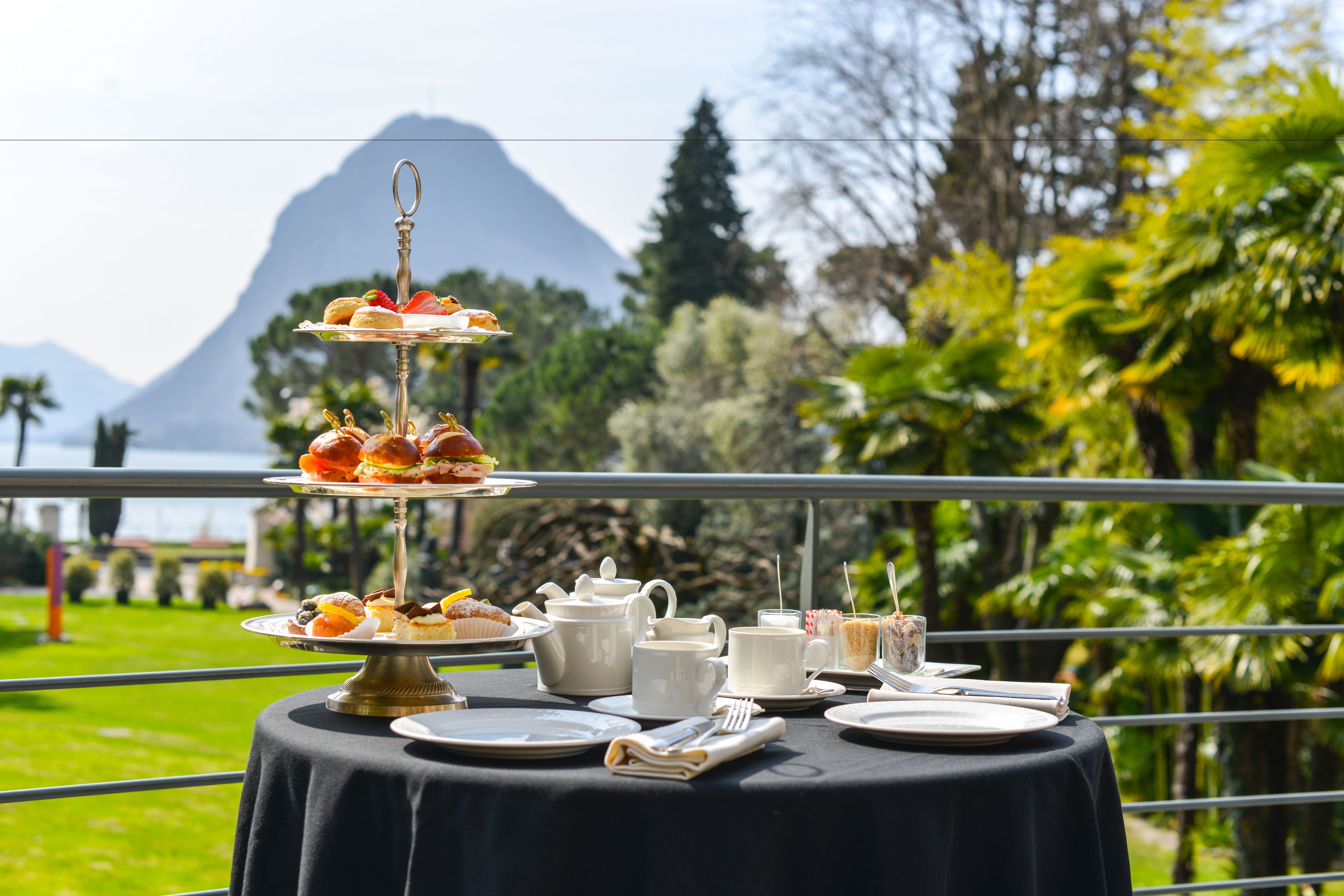 A table set outdoors with a tiered dessert display, white tableware, and a scenic mountain view.