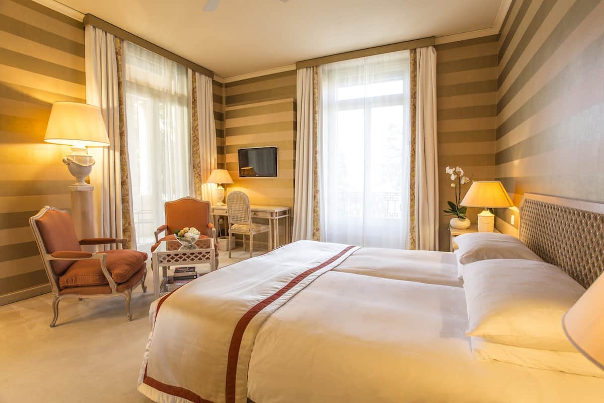 Habitación de hotel con una cama grande, dos mesitas de noche, una silla, un escritorio y un televisor en la pared.
