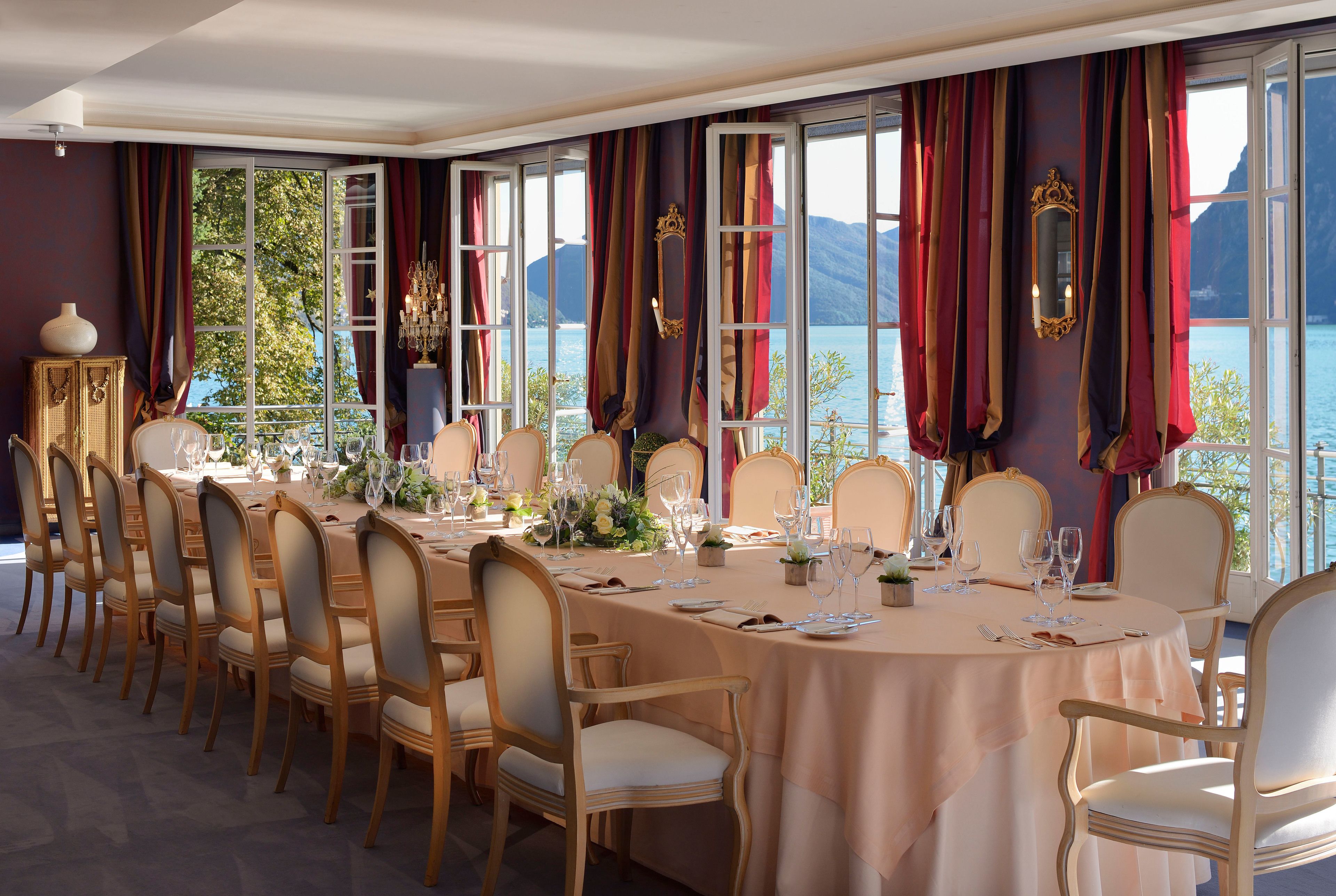 Una sala da pranzo formale con un lungo tavolo apparecchiato per un pasto, ampie finestre con tende e vista sull'acqua e sulle montagne.