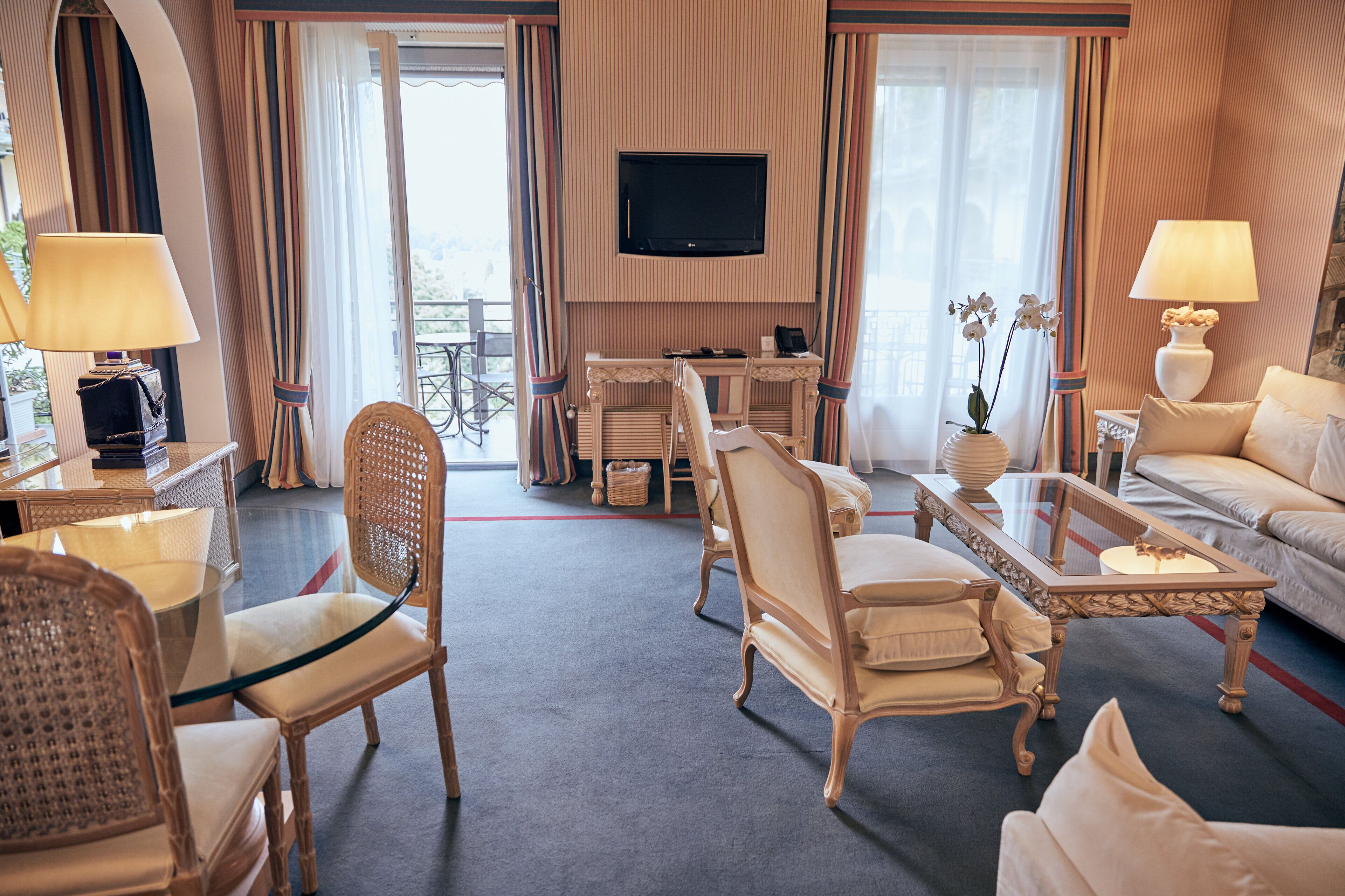 Une chambre d’hôtel équipée d’un téléviseur fixé au mur, d’un canapé, de deux fauteuils, d’une table basse et d’une table à manger avec des chaises.