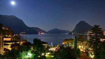 Vista noturna de um lago com montanhas ao fundo, edifícios iluminados e céu claro.