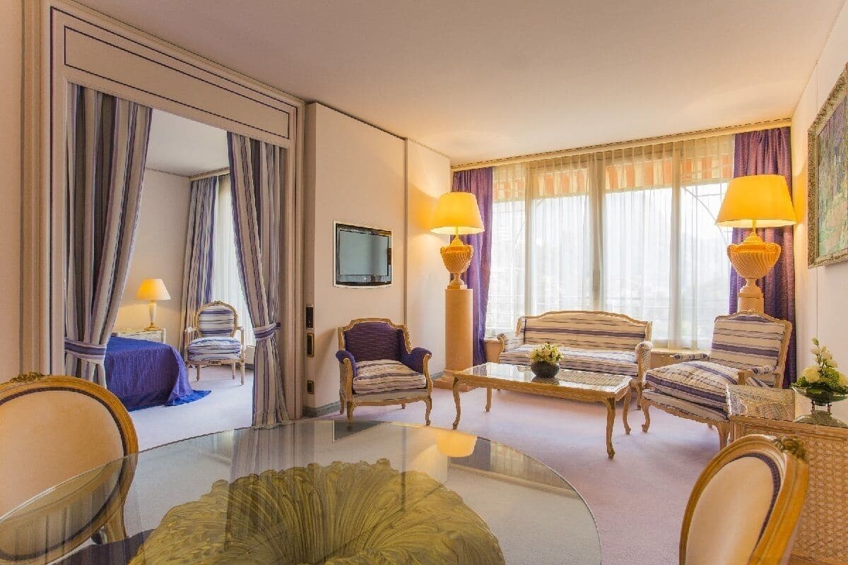 Una habitación de hotel con una mesa de vidrio, sillones a rayas, un sofá y un televisor.