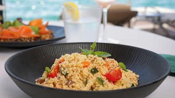 A bowl of couscous salad with a lemon slice garnish, a glass of white wine, and a plate of salmon on toast.
