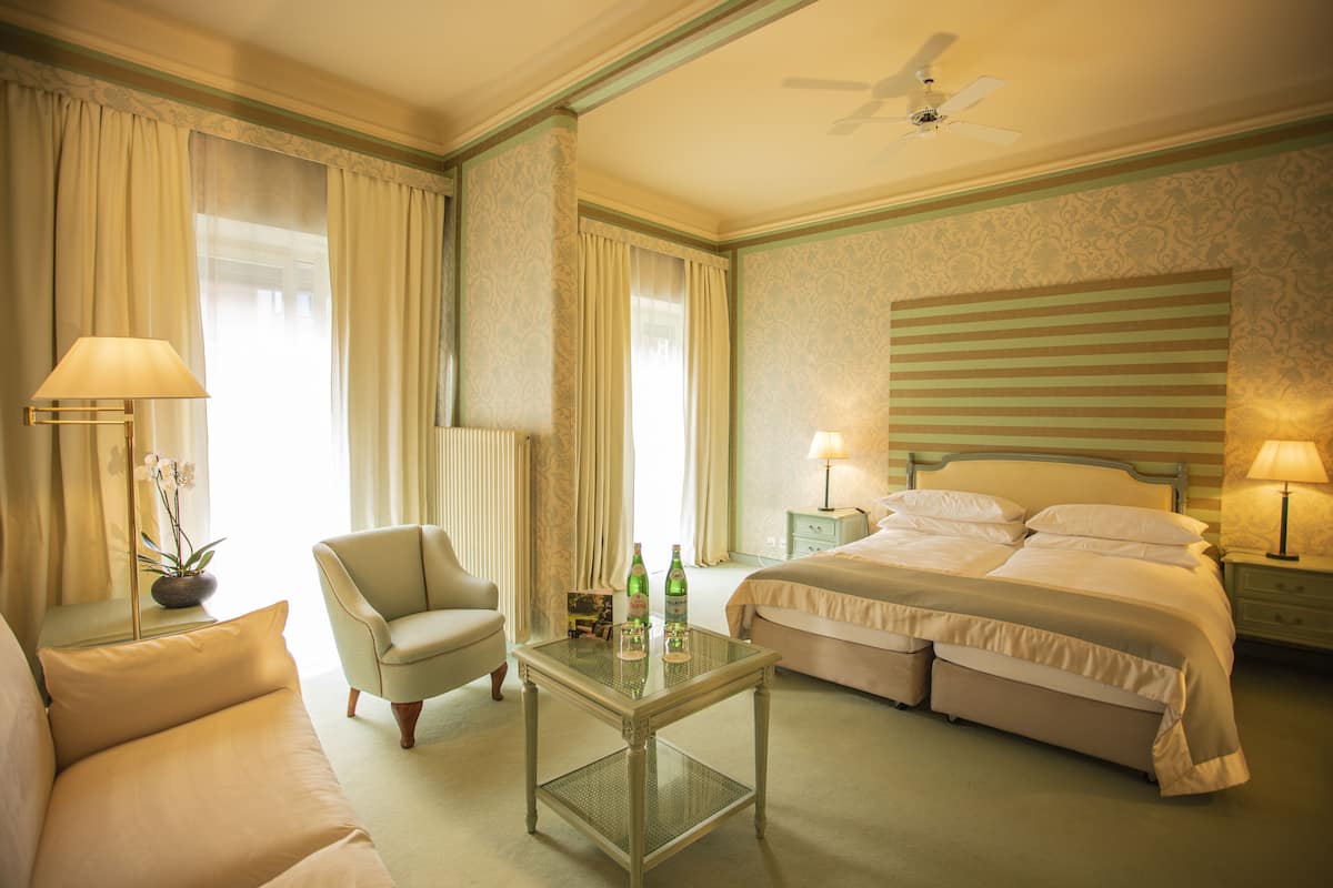 Habitación de hotel con cama, una silla, una mesa con botellas y un ventilador de techo.