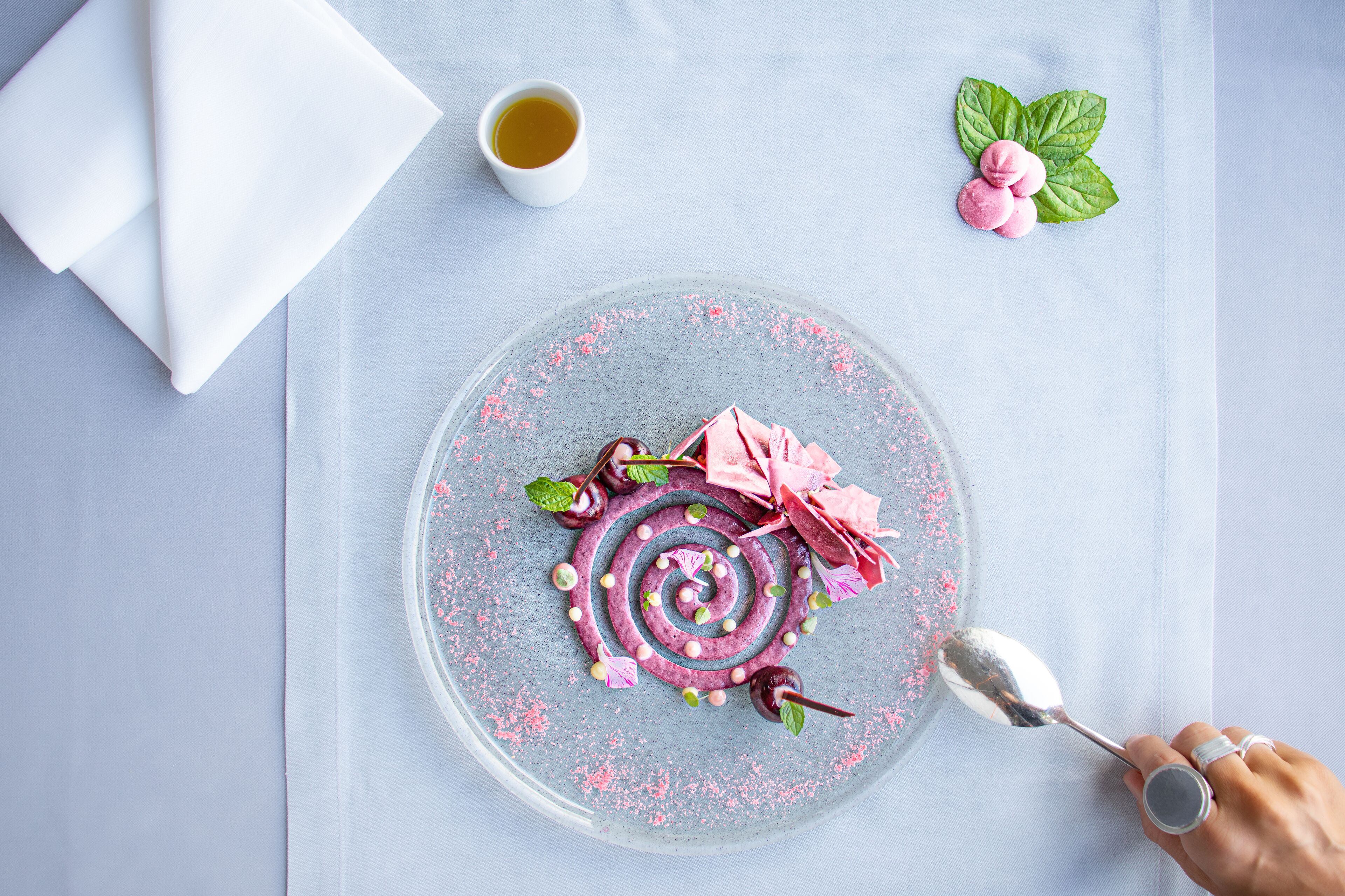 Een dessert op een helder bord met roze en groene accenten, een klein kopje thee en muntblaadjes.