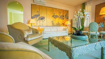 Ein Wohnzimmer mit einer Couch, Sesseln, einem Glastisch und einem großen Gemälde an der Wand.