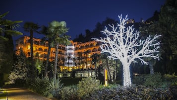 Ein gut beleuchtetes Hotel mit einem markanten, mit Lichtern geschmückten Baum, umgeben von üppiger Vegetation und Palmen.