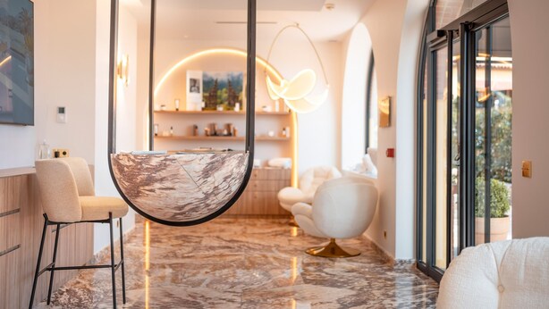 A modern interior with a marble floor, a hanging light fixture, and a seating area with a white chair and sofa. - Ermitage de l'Oasis & Spa - Cannes Mandelieu (Mandelieu-La-Napoule)