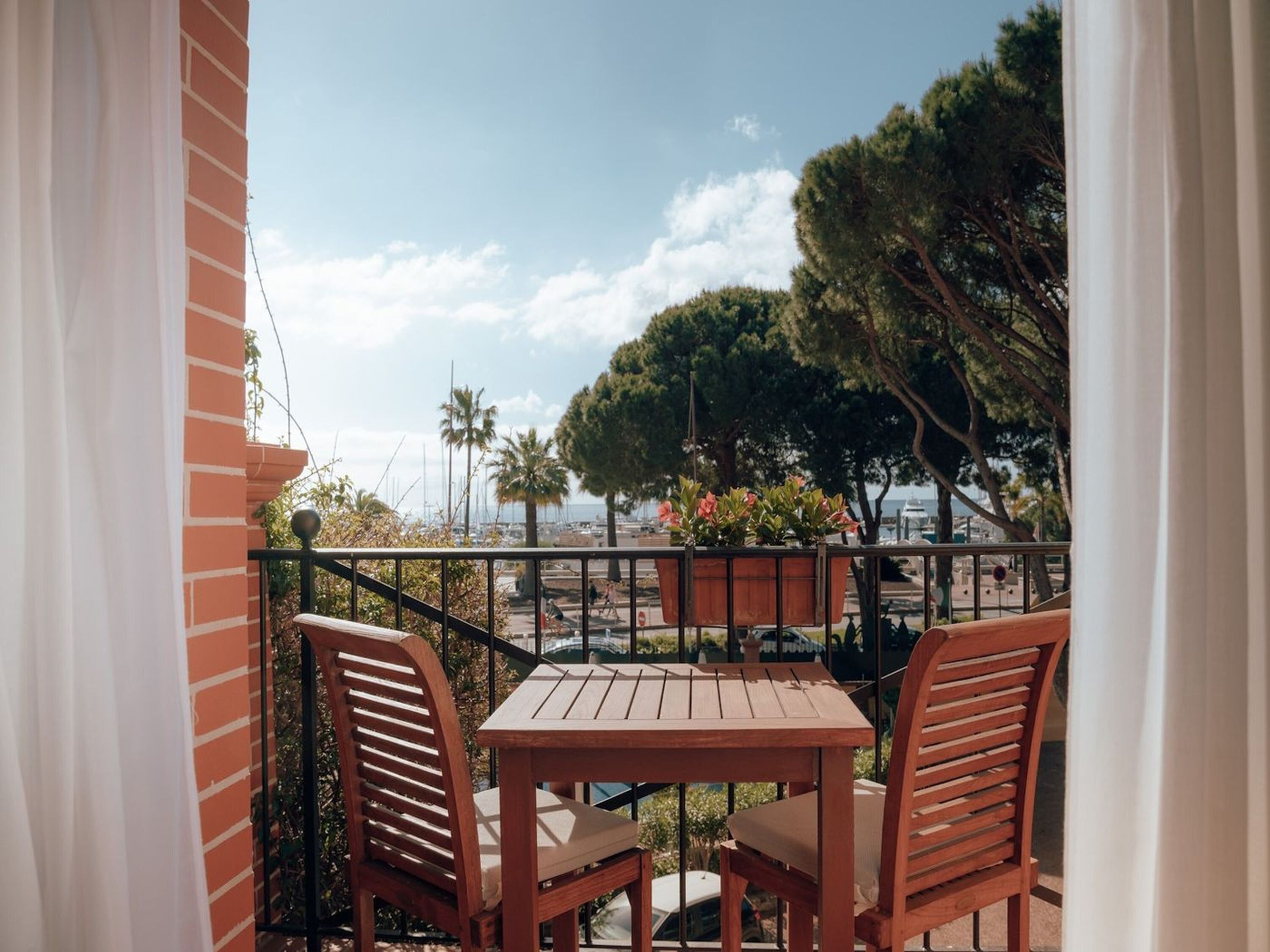 A balcony with a wooden table and two chairs, overlooking a marina with boats and trees.