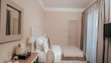 A hotel room with a bed, a desk with a coffee maker, a chair, a TV, and curtains.