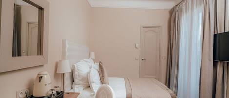 A hotel room with a bed, a desk with a coffee maker, a chair, a TV, and curtains.