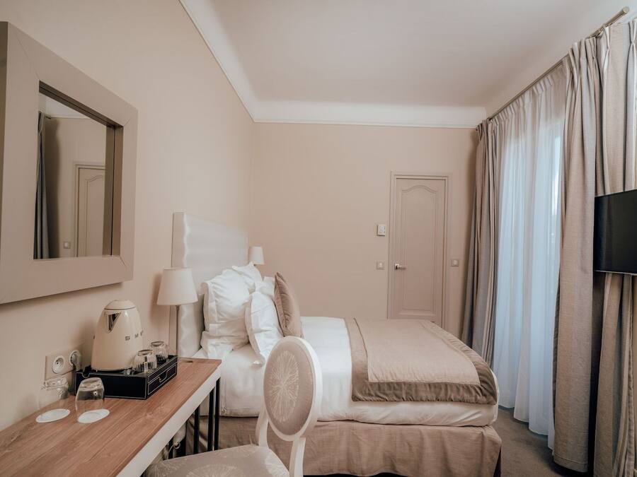 A hotel room with a bed, a desk with a coffee maker, a chair, a TV, and curtains.