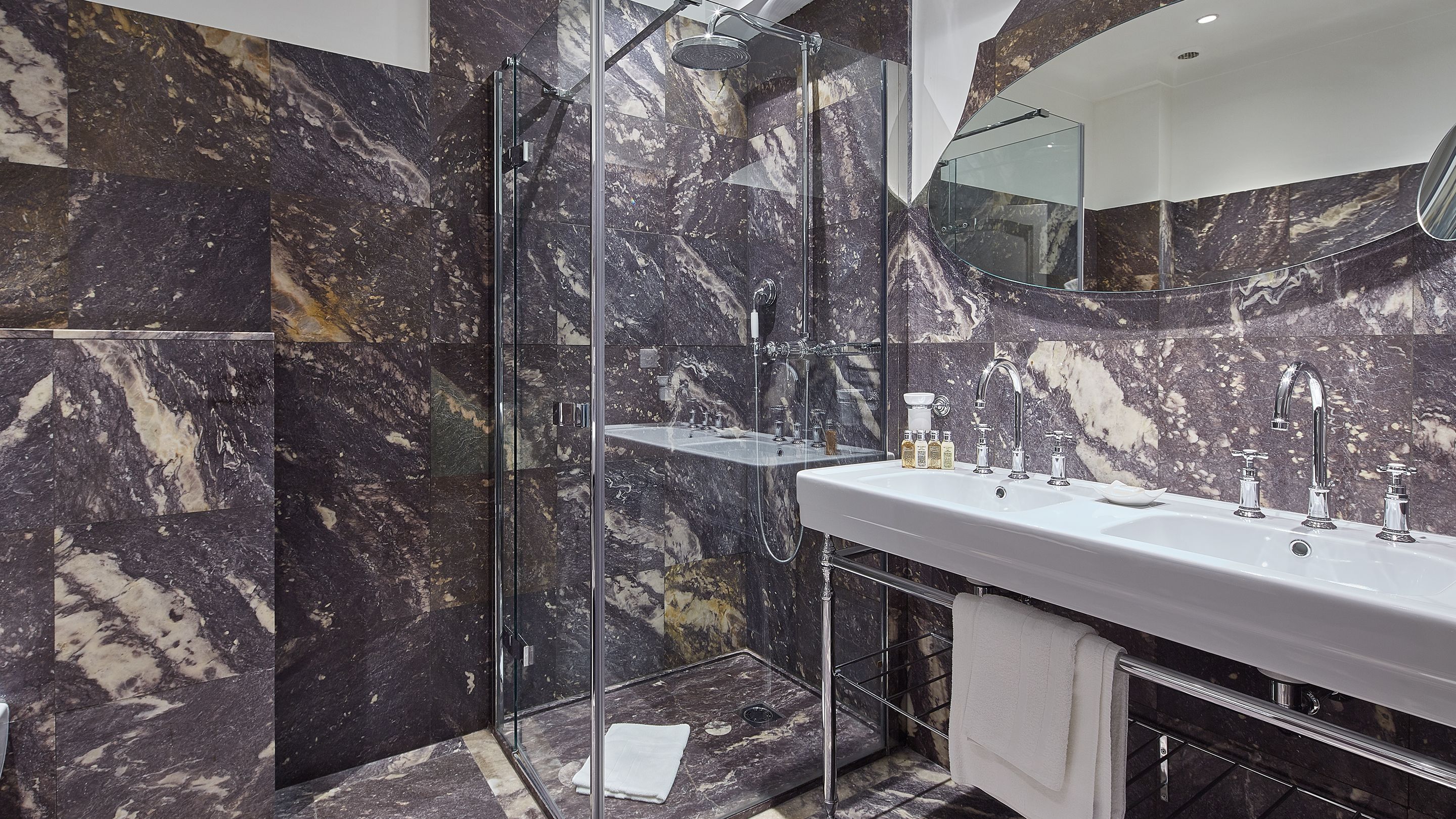 Un baño moderno con ducha de vidrio, un tocador espacioso con espejo y paredes de mármol.