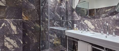 Un baño moderno con ducha de vidrio, un tocador espacioso con espejo y paredes de mármol.