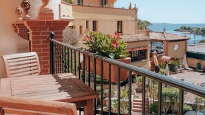 A balcony with a wooden table and chairs, potted plants, and a view of a building and the sea. - Ermitage de l'Oasis & Spa - Cannes Mandelieu (Mandelieu-La-Napoule)