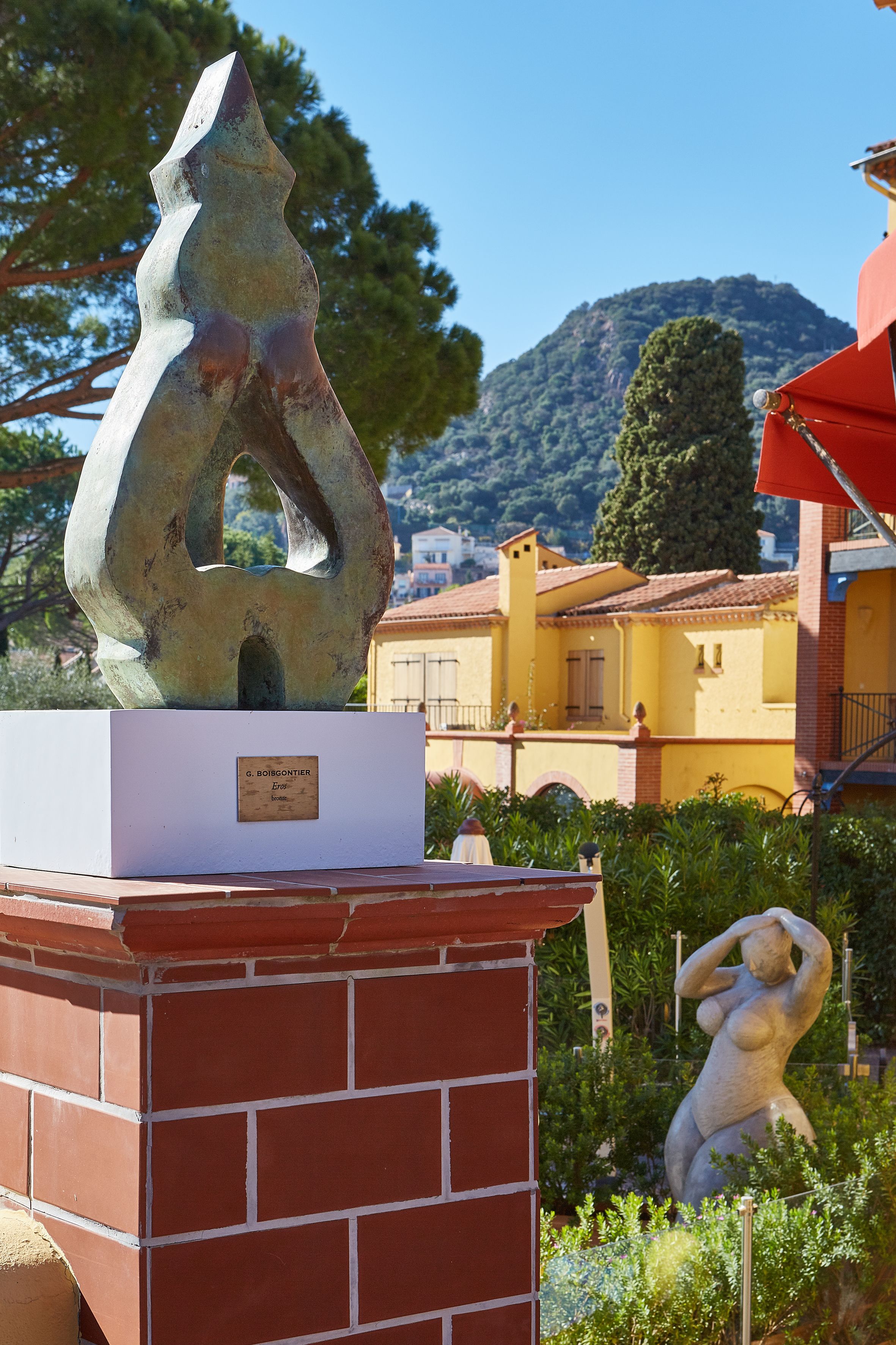 A sculpture on a pedestal in a garden with a mountain in the background.