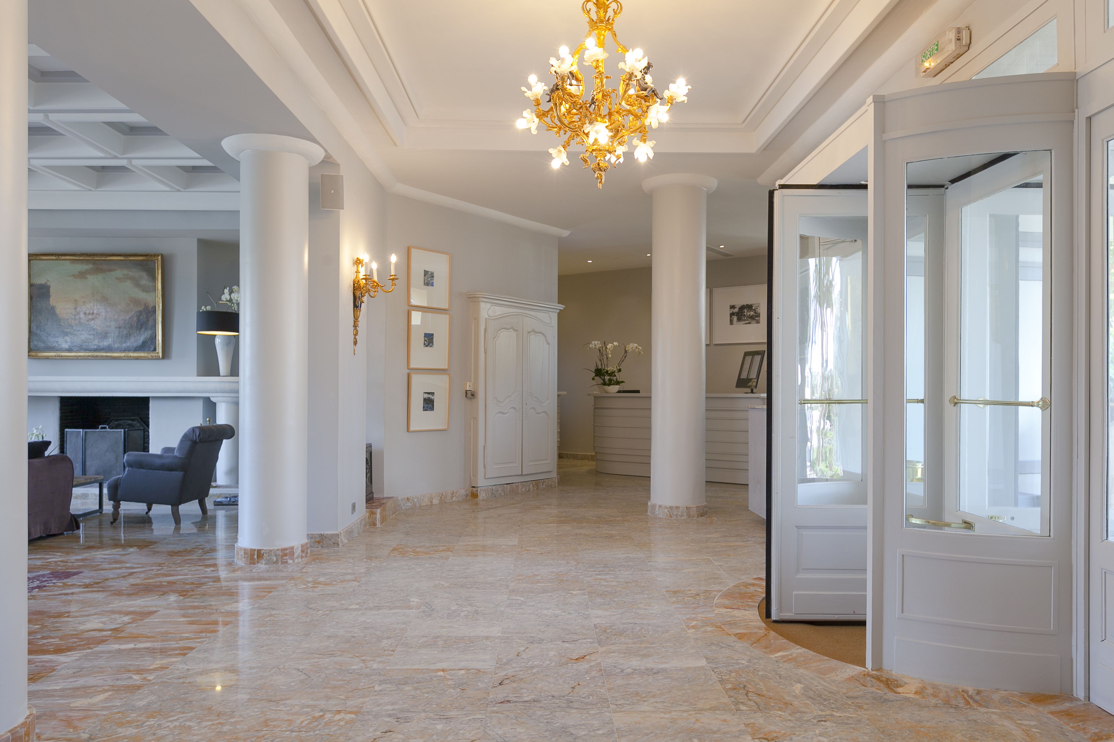 A spacious lobby with marble flooring, white columns, a chandelier, and a seating area with a fireplace.