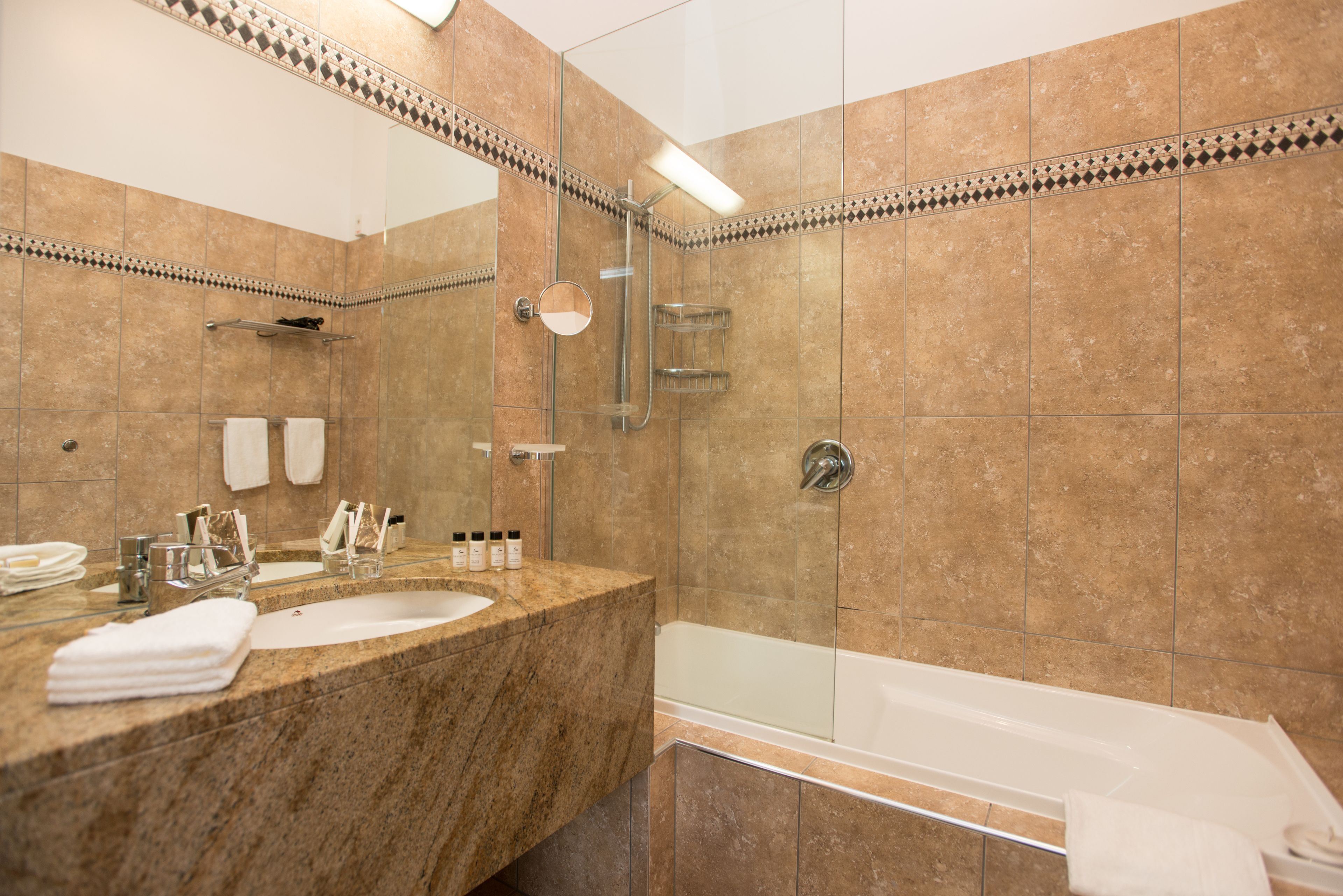 Un baño con lavamanos de mármol, ducha con mampara de vidrio y bañera.