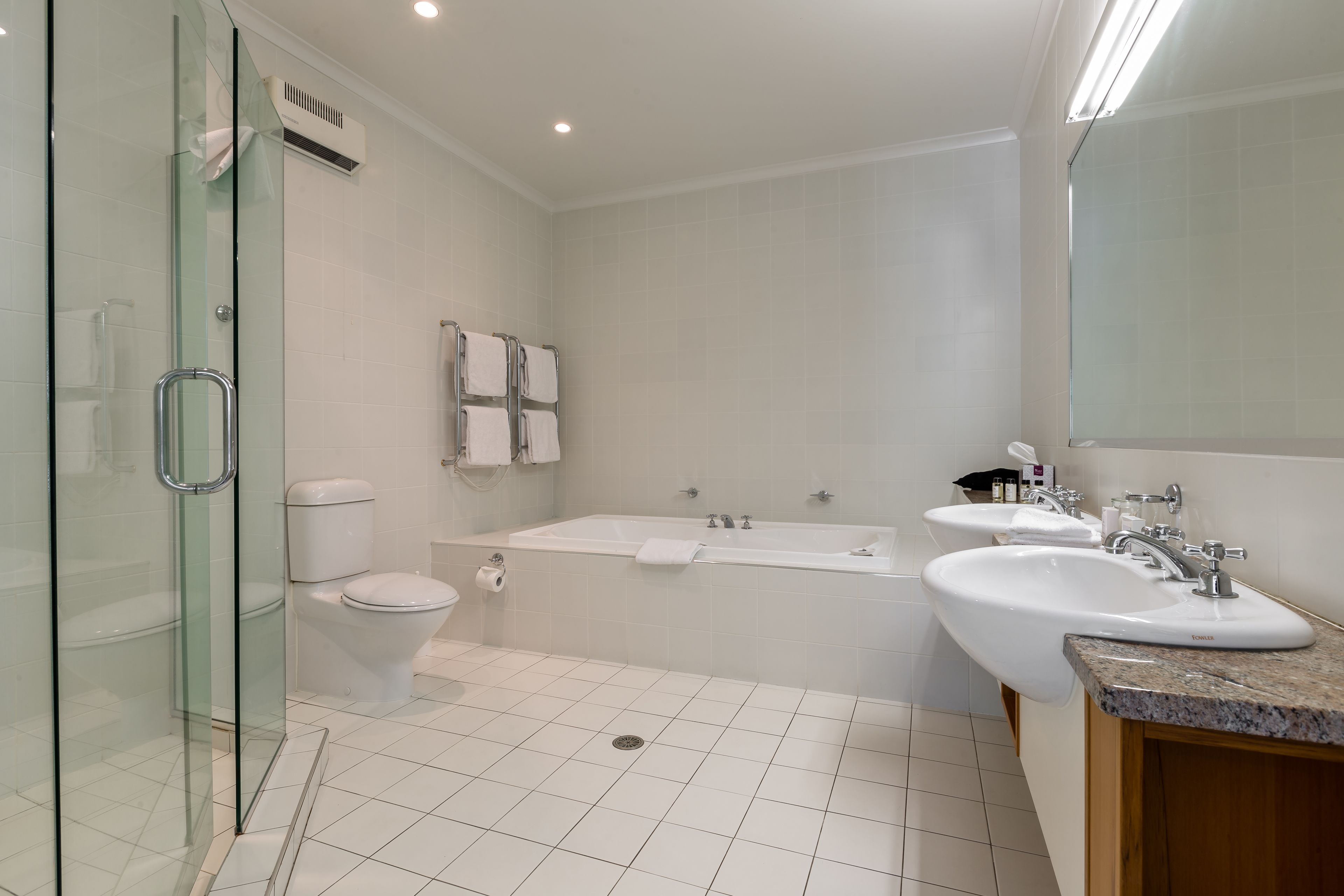Un baño moderno con cabina de ducha de vidrio, inodoro, bañera y dos lavabos.
