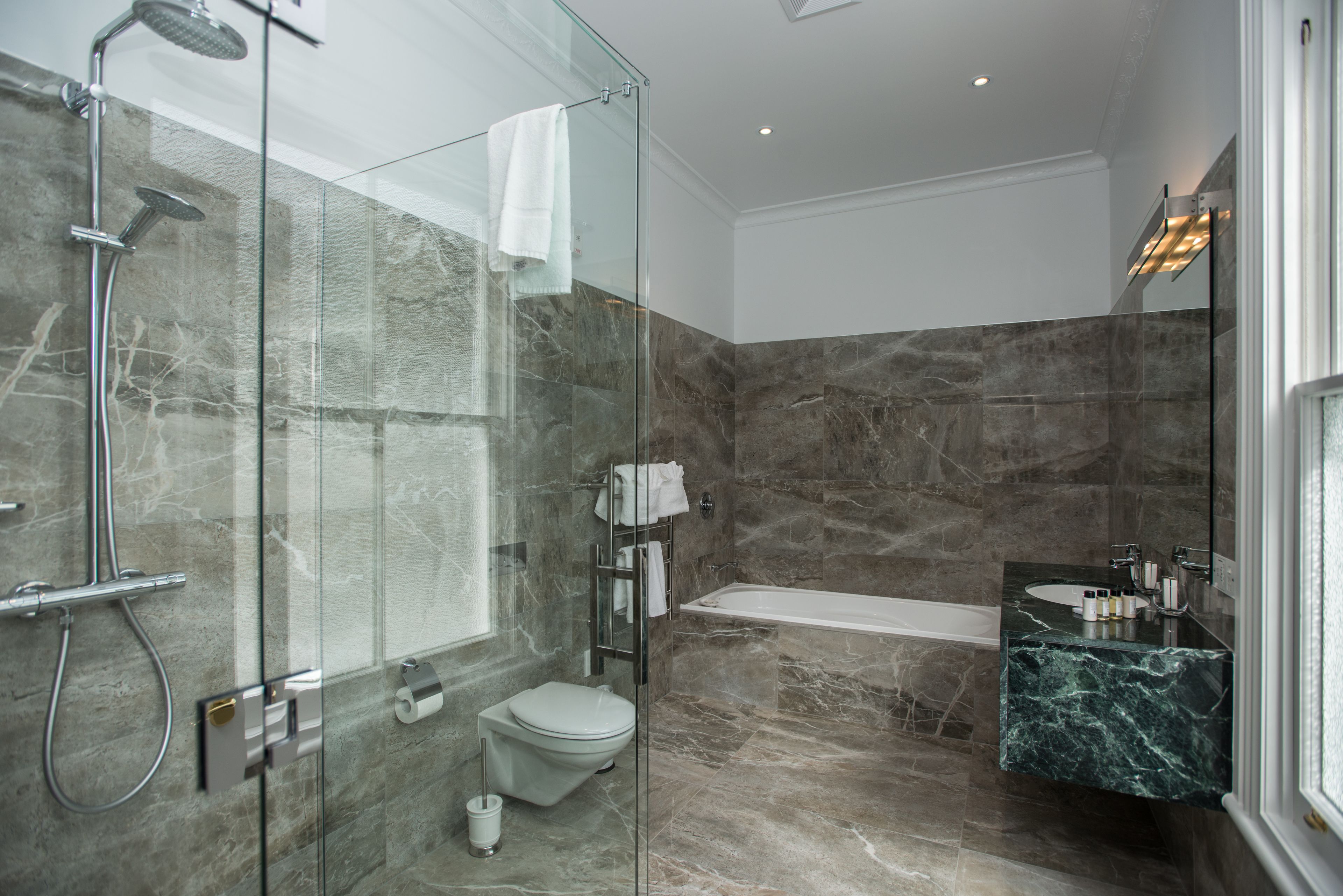 A modern bathroom with a glass-enclosed shower, a toilet, a bathtub, and a marble countertop sink.
