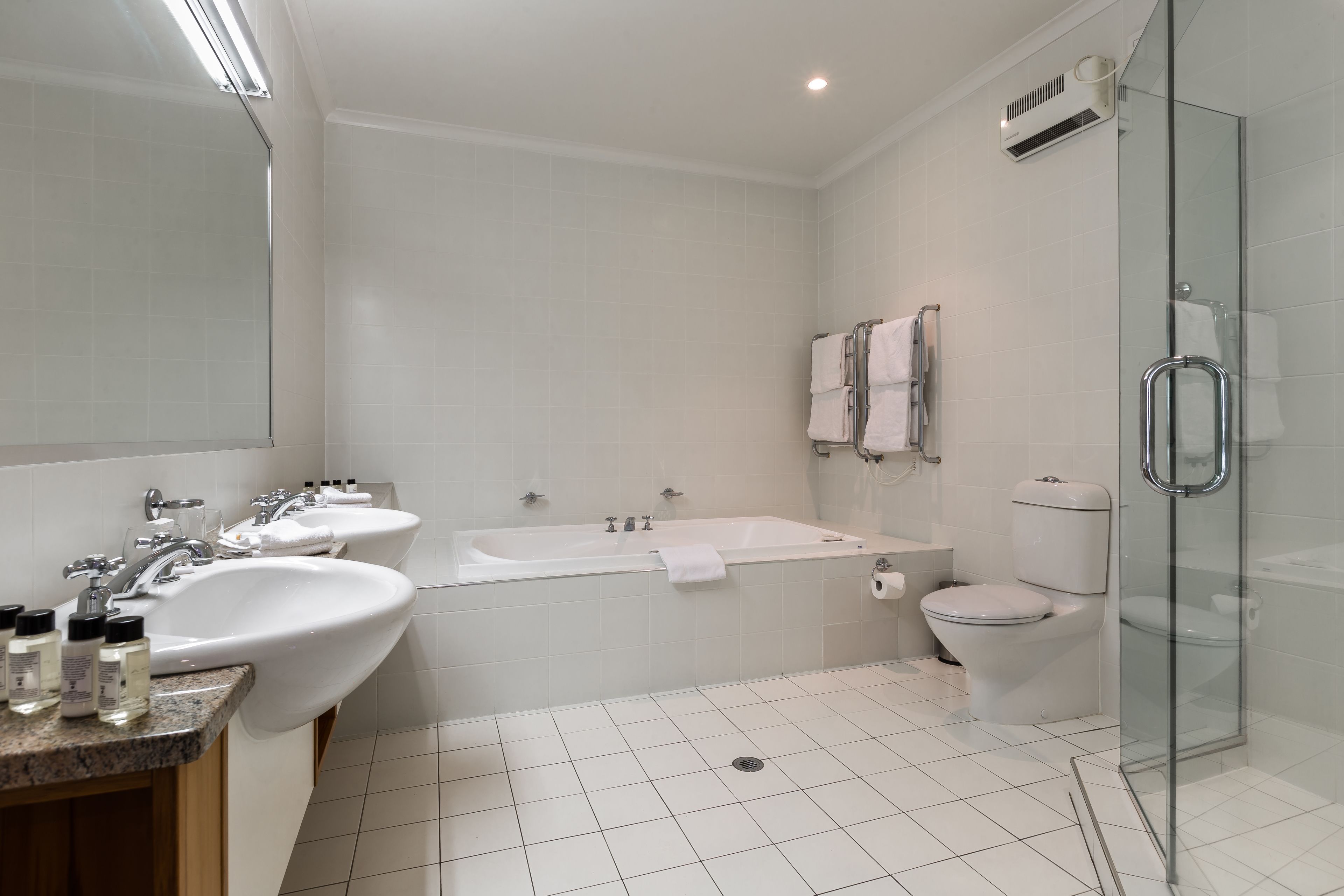 A modern bathroom with two sinks, a bathtub, a toilet, and a glass shower enclosure.