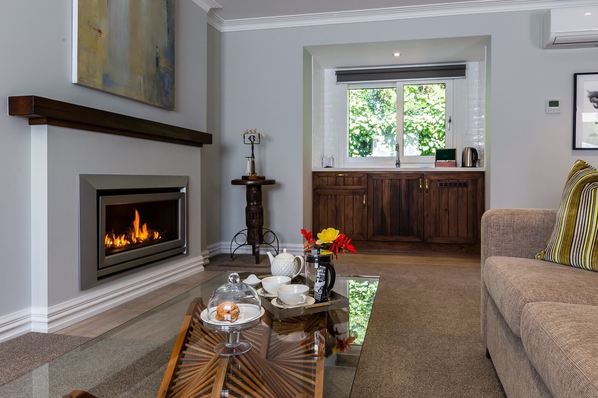 A living room with a fireplace, a dining table with a tray of food and drinks, a sofa, and a kitchen in the background.