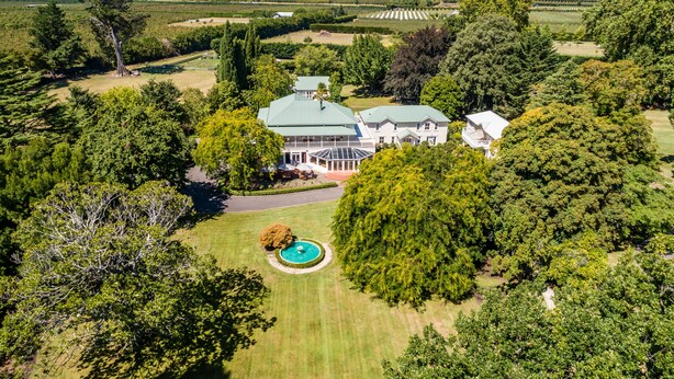 Vista aérea de una extensa propiedad con una casa principal, jardines amplios y una piscina.