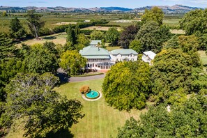 Vista aérea de una extensa propiedad con una casa principal, jardines amplios y una piscina.
