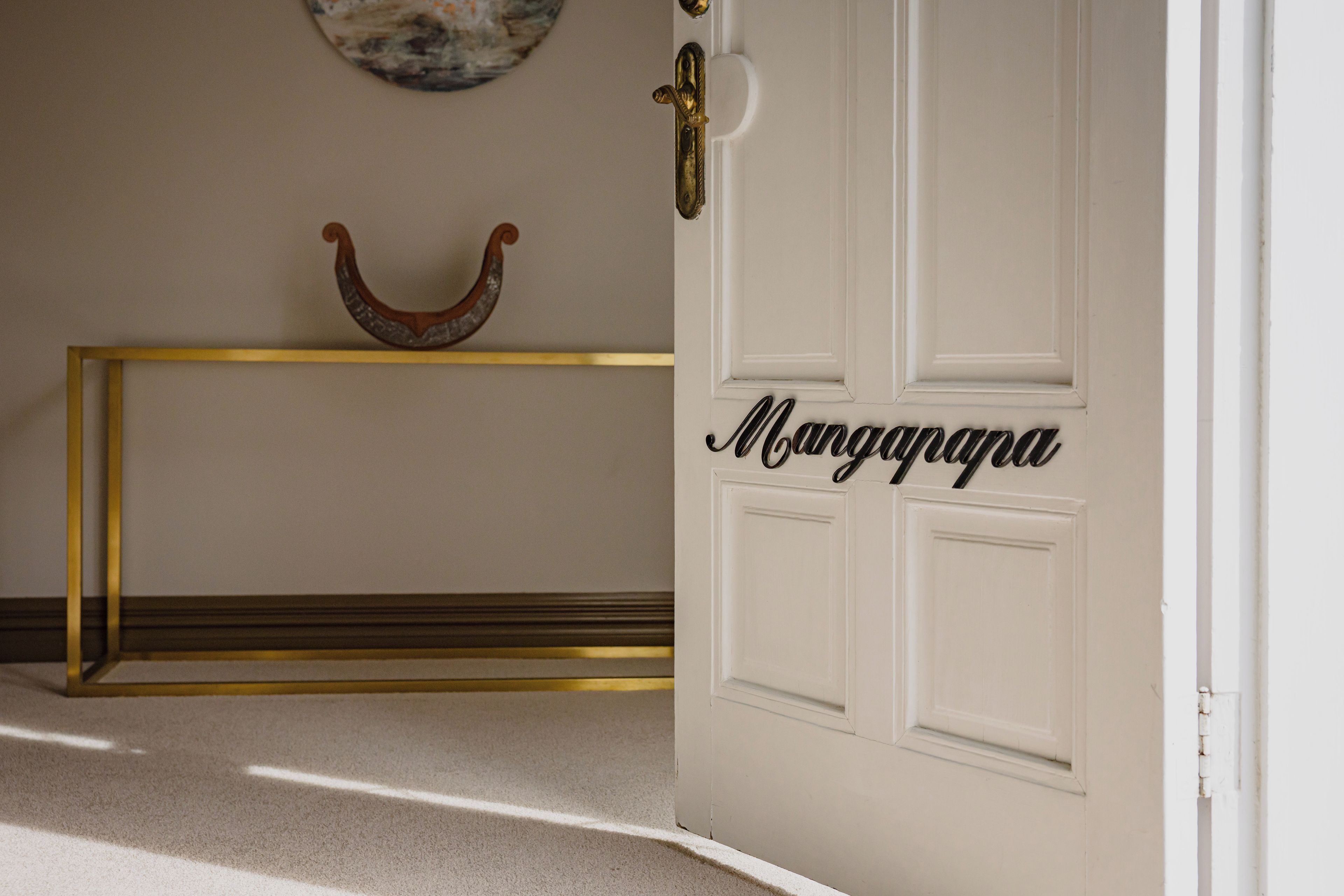A white door with a nameplate reading 'Mangapa' and a gold-colored console table with a decorative object on top.