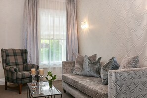 A living room with a plaid armchair, patterned sofa, and a glass coffee table with candles and a vase. - Mangapapa Hotel (Havelock North)