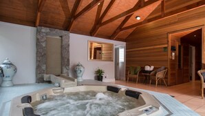 Un jacuzzi en una cabaña de madera con paredes de piedra, un espejo y mobiliario de mimbre.