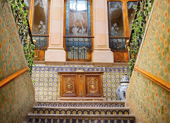 A staircase with ornate blue and yellow patterned tiles, wooden balustrades, and decorative metal railings.