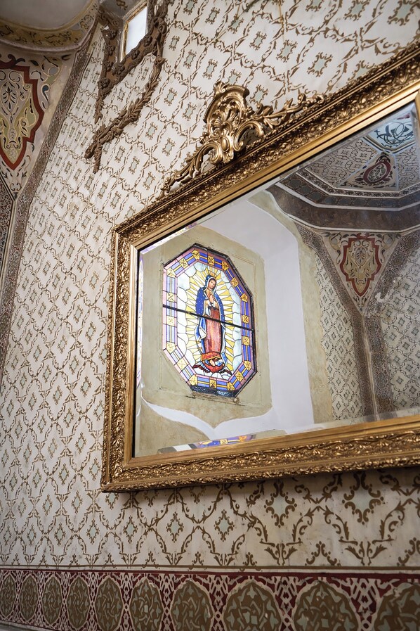 A room with ornate wallpaper, a large framed stained glass window, and a decorative ceiling.