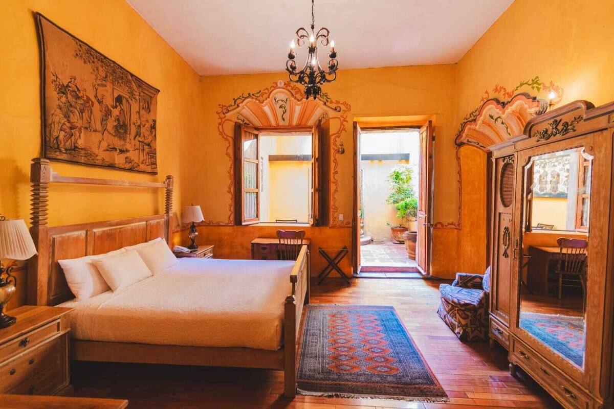 Una habitación tradicional con cama, muebles de madera, un candelabro y un espejo grande.