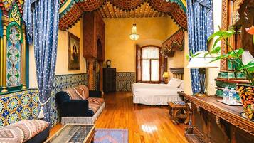Una habitación tradicional con sofá, cama, mesa de centro de madera y una lámpara decorativa.