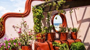 A patio with a table and chairs, surrounded by terracotta pots with plants, a curved wall, and a view of the sea. - La Casa de la Marquesa (Querétaro)