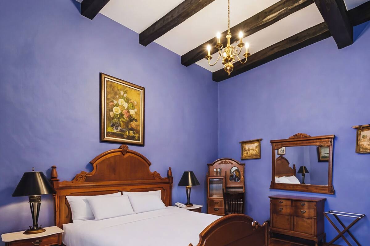 Un dormitorio con cama de madera, mesita de noche, cómoda, espejo y candelabro.