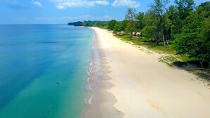 Una extensa playa de arena con agua turquesa cristalina y una hilera de árboles a la derecha.