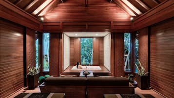 A wooden interior with a central seating area, large windows, and a ceiling with wooden beams.