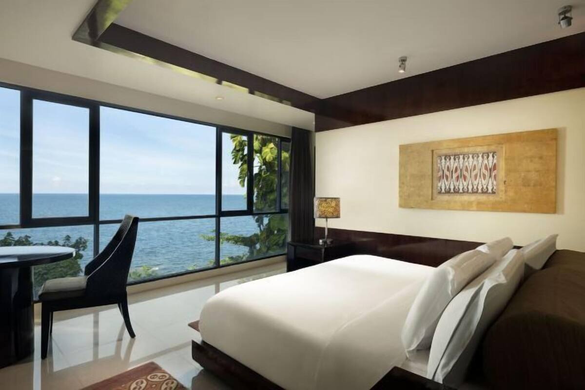 A bedroom with a large window, a bed, a chair, and a table.