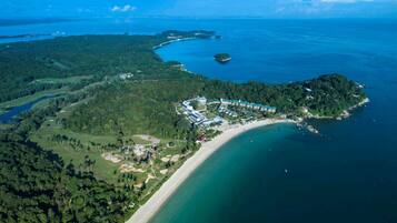 An aerial view of a coastal resort with a beachfront, dense forested areas, and a marina.