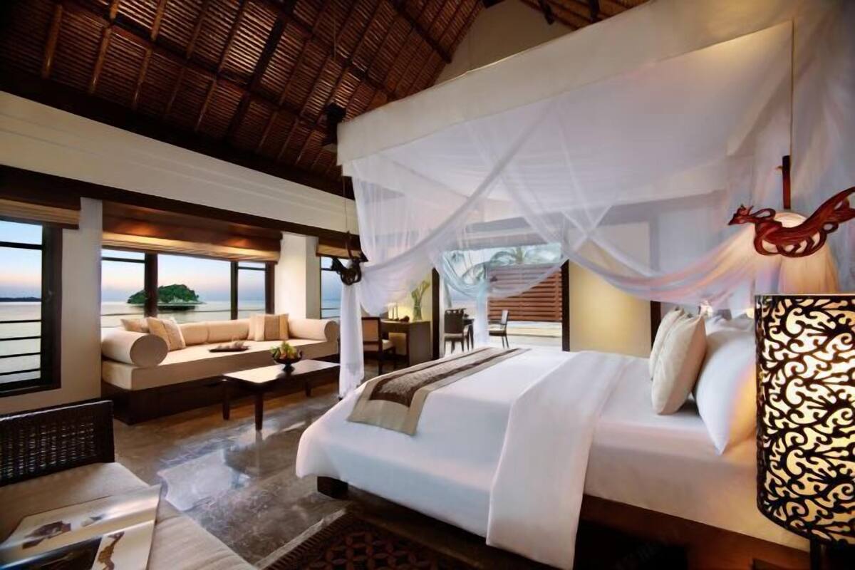 A bedroom with a bed, a sofa, a desk, and a view of the sea.