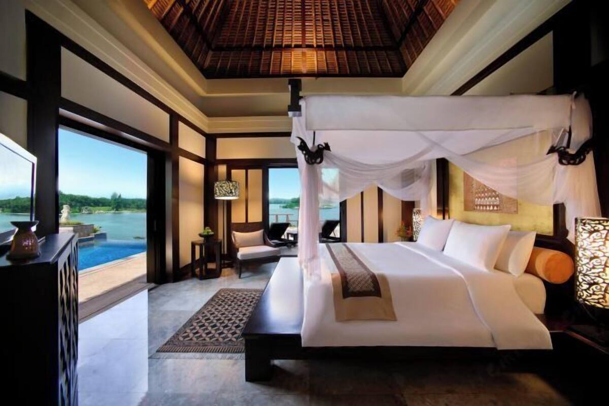 A bedroom with a large bed, a canopy, a view of a body of water, and a pool.